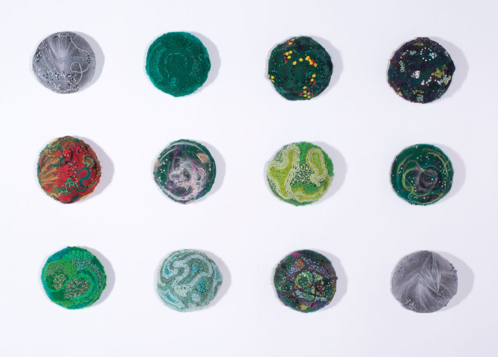 Juliet Karelsen, Small Nature Domes (grid of 12), embroidery floss, thread, wool fibers, wool, and paper on felt, stuffed with fiber fill and mounted on wood, 5” diameter each, grid approximately 30” x 40”, 2017–2018