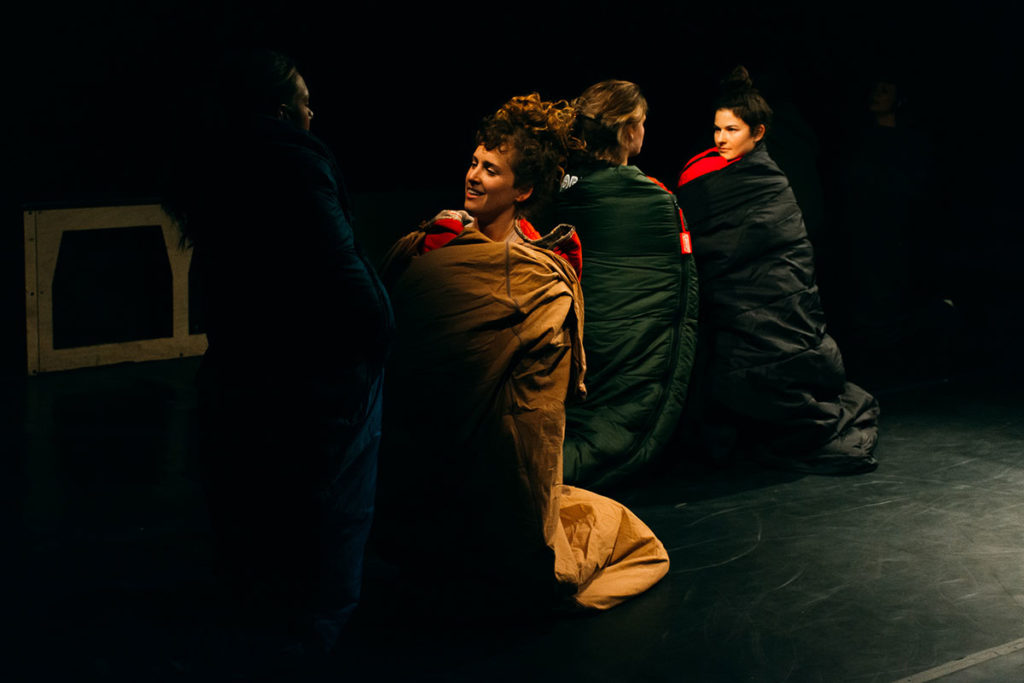 Four dancers (performers and audience members) are in two pairs on the dance floor. Everyone is wrapped in a sleeping bag. Each pair of people are on their knees and looking into each others' eyes.