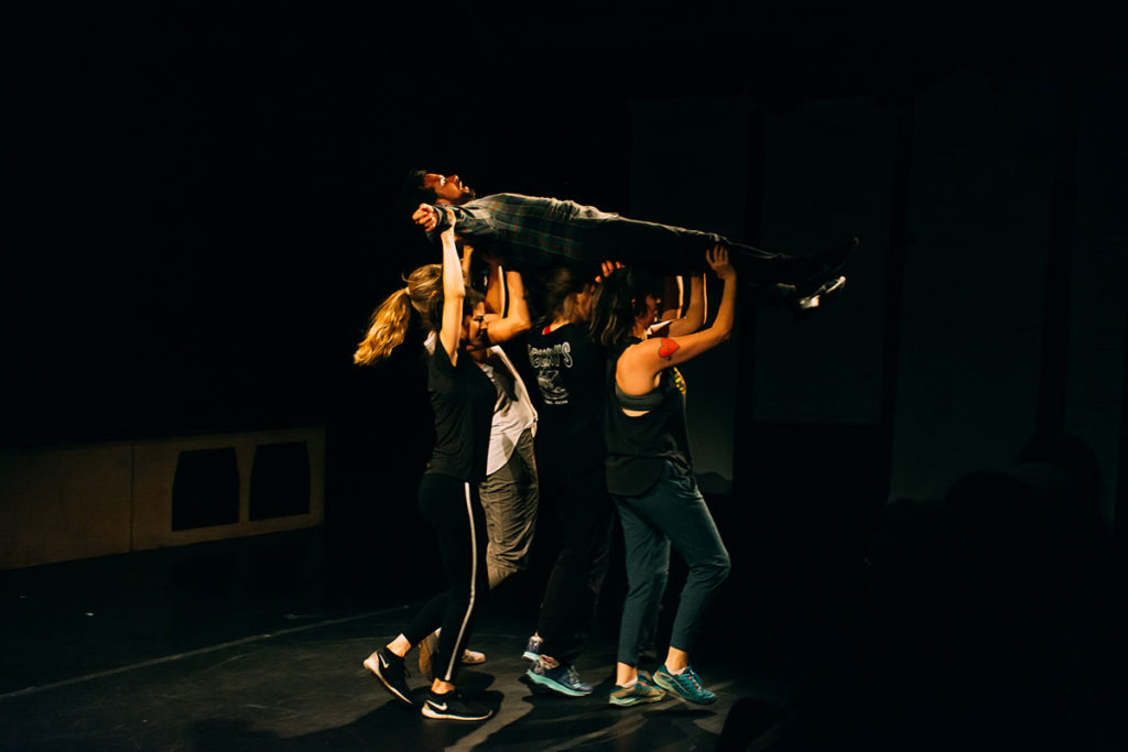Four women carry a man above their heads. The way he is holding his body, he looks as if he is either crucified or crowdsurfing.